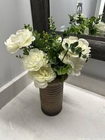 Front view of artificial white flowers in brown textured vase on countertop with mirror background.