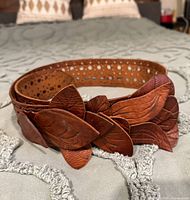 Close-up of the brown leather belt showing perforations along the strap and leaf-shaped leather decorative elements.
