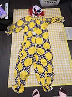 Full view of clown jumpsuit laid flat on a checked yellow and white mat with ruler for scale.