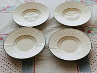 Four white saucers viewed from an angle showing embossed patterns and rim design.