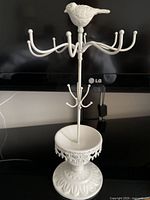 Full front view of the white rustic jewelry stand showing multiple rounded hooks for hanging jewelry and the bird figure on top.