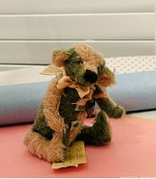 Small vintage handmade mohair teddy bear, beige and green color, sitting height about 10 cm. Shows tag and detailed face and paws.