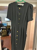 Black button-up dress with short puffed sleeves and gold buttons on green hanger, background shows room interior