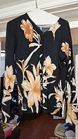 Black floral print cardigan shown hanging on white hanger, long-sleeved with vibrant large floral pattern