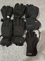 Five pairs of black winter gloves on a gray carpet, including four heavy-duty Burton gloves and one lighter Roots glove.