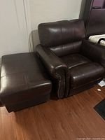 Brown leather armchair with matching ottoman side by side on hardwood floor, showing general appearance and condition.
