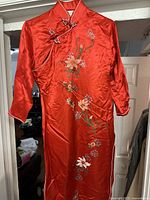 Red Chinese silk dress hanging on door showing full front embroidery and traditional collar with frog buttons