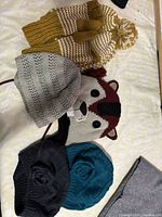 Photo of 5 knit hats including striped pom-pom, character face, and solid colors with knit patterns.