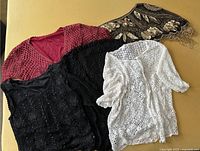 Four lace sweaters in white, black (two styles), and maroon, plus one embellished shawl with leaf designs.