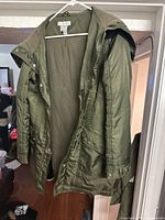 Front view of the medium green synthetic jacket hanging on a hanger, showing buttons, collar, and sleeves.