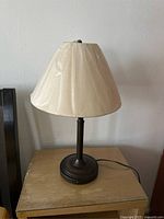 Bedside lamp with beige fabric shade covered with plastic, showing lamp base and cord.