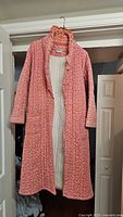 Front view of the pink quilted robe hanging on a hanger showing full length with visible front pockets and ruffled collar.
