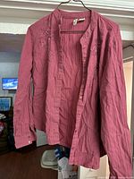 Front view of red cotton button-up shirt with embroidery on display hanging on a hanger.