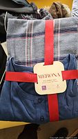 Folded blue Henley pajama shirt with button detail and plaid pajama pants tied with red ribbon, with Merona tag showing size XL and fabric content.