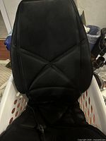 Front view of the Relaxo black gel chair back massager placed on a white laundry basket, showing ergonomic design and black gel outer material.