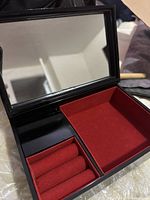 Open jewelry box showing velvet-lined compartments with ring rolls and mirror inside lid.
