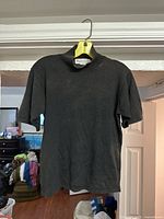 Photo of black short sleeve sweater hanging on yellow hanger, showing front view.