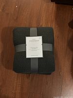 Folded Threshold Sweater Knit Blanket in dark gray with label showing brand and product details, placed on wooden floor.