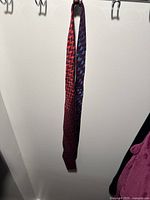 Front view of a long red silk tie with a repeating geometric cube pattern in red and dark blue hanging from hooks.