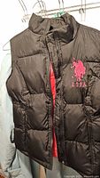 Front view of black puffer vest showing pink US Polo embroidered logo and front zipper.