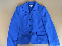 Women's blue blazer laid flat showing full front view with collar, button closures, and flap pockets.