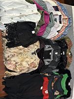 Photo showing mixed women's tops including black lace blouse, floral satin blouse, and other colorful tops laid out side by side.