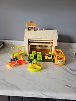 Full set photo showing red schoolhouse with green desks, figures, yellow bus, and playground equipment in front on white surface.