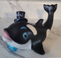 Front side view of the Marineland Kandu Killer Whale piggy bank showing the painted ceramic figure with top hat and bow tie.