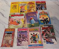 Photo showing a variety of 12 vintage books and comics including Heathcliff, Dennis the Menace, Mad, Gargoyles, Paddington, Power Rangers, Conan, Girl Talk, and Adventures magazines.