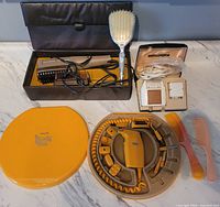 Overview photo showing Remington shaver, Phillips manicure set in orange case, Shick hair dryer, two wet combs, and hairbrush.