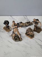 Seven MacFarlane military figures in desert and black tactical gear posed on a flat surface with bases simulating terrain.