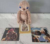 Photo showing original 1982 E.T. plush seated with three E.T. books on a flat surface under natural light.