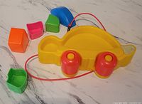 Yellow turtle-shaped pull-along toy with red wheels and a red string, assorted colorful puzzle pieces of various shapes around it.
