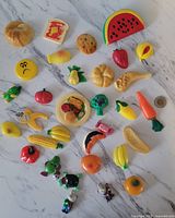 Overhead photo of 31 assorted vintage 1980s plastic fridge magnets shaped as various foods and several character figures, showing condition and details with a twoonie coin for size reference.