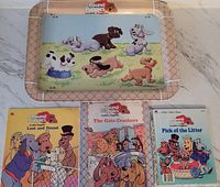 Top-down view showing metal TV tray with cartoon Pound Puppies puppies and three Pound Puppies books beneath