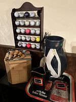 Golf themed bar decor setup with golf bag, shelf with golf balls, wooden box with golf tees, and Carling Black Label branded tray and pitcher.