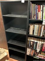 Front view of black wooden bookcase with five shelves, showing adjustable shelf holes on sides and visible wear/dust on shelves.