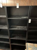 Front view of the black bookshelf showing adjustable shelves and some wear.