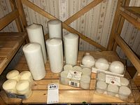 Overview of various white candles of different sizes, including tall pillar candles and packed smaller votive candles.