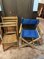 Overview photo showing one blue fabric director's chair next to three wooden folding chairs leaning against a dark wood background.