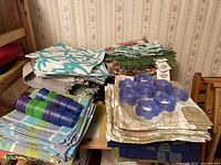 Multiple stacks of assorted cloth napkins in various colors and patterns including marine and plaid designs, with two sets of plastic napkin rings in blue and green placed on top.