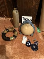 Photo showing full set of miscellaneous decor including the earthen bottle, ceramic frog, circular ceramic ornament, glass eye charm and orca tile art.