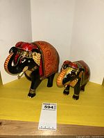 Two hand-painted elephant figurines, larger elephant about 8 inches tall, showing front and side view with intricate gold and red patterning