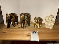 Set of four figurines including three painted elephants and one white Ganesha statue placed on wooden shelf