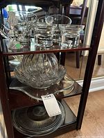 Shelf display showing three small clear glass bowls with pedestal bases, a large swirl-pattern clear glass bowl, and a large round clear glass serving tray on bottom shelf.