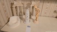 Six items including Roman Coliseum model, Tower of Pisa model, two Greek columns about 10 inches tall, and statue of Greek lady on a flat surface