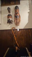 Four wooden masks wall mounted with a carved wooden cane leaning against the wall below