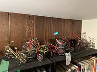 Wide view of the 7 miniature bicycles arranged on black shelving against wooden wall.