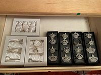 Drawers holding multiple sets of crown-shaped napkin rings and diamond ring holders arranged in black and white display boxes