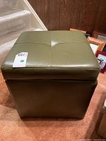 Front view of the green-grey square ottoman showing stitched top and synthetic leather upholstery.